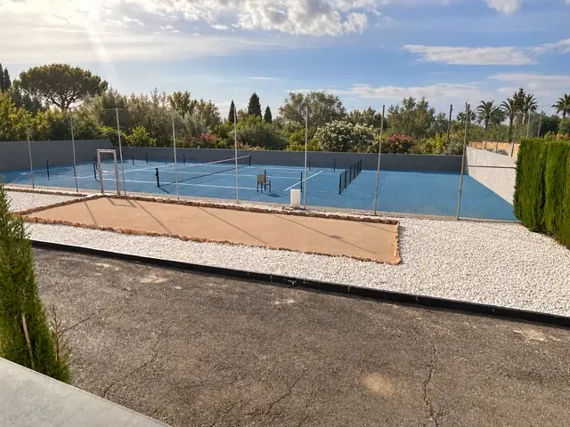 Blauwe tennisbaan met vernieuwde voorgrond en wit grind; achtergrond digitaal vervangen door mediterraan groen